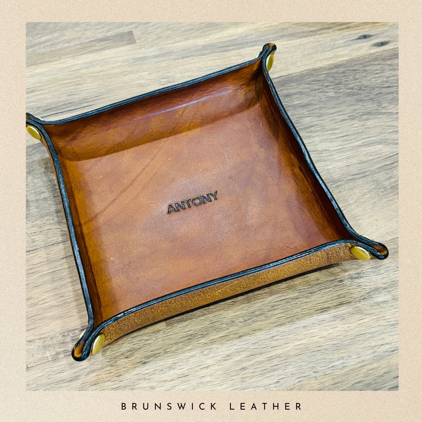 Brown leather tray with 'ANTONY' branding on a wooden surface, branded 'Brunswick Leather'.