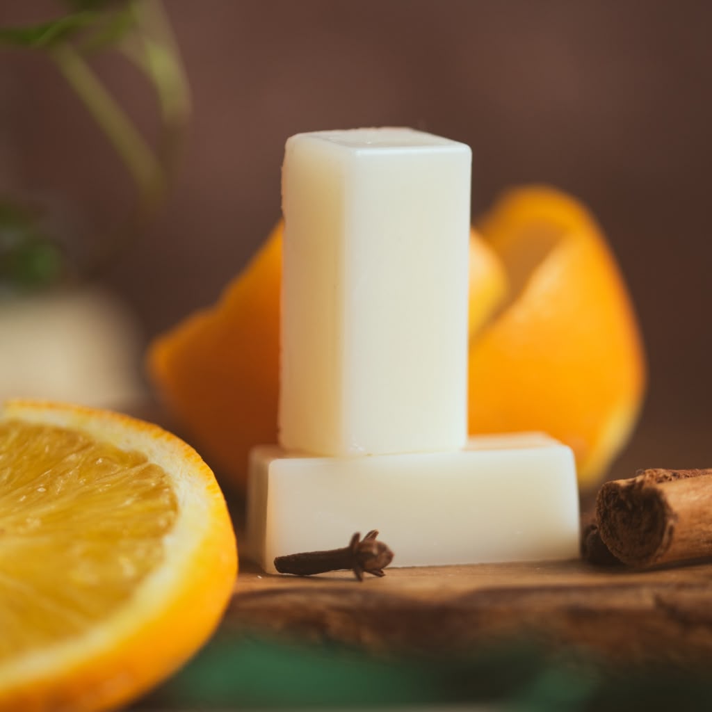 Two wax melts on a wooden surface with oranges and cinnamon sticks.
