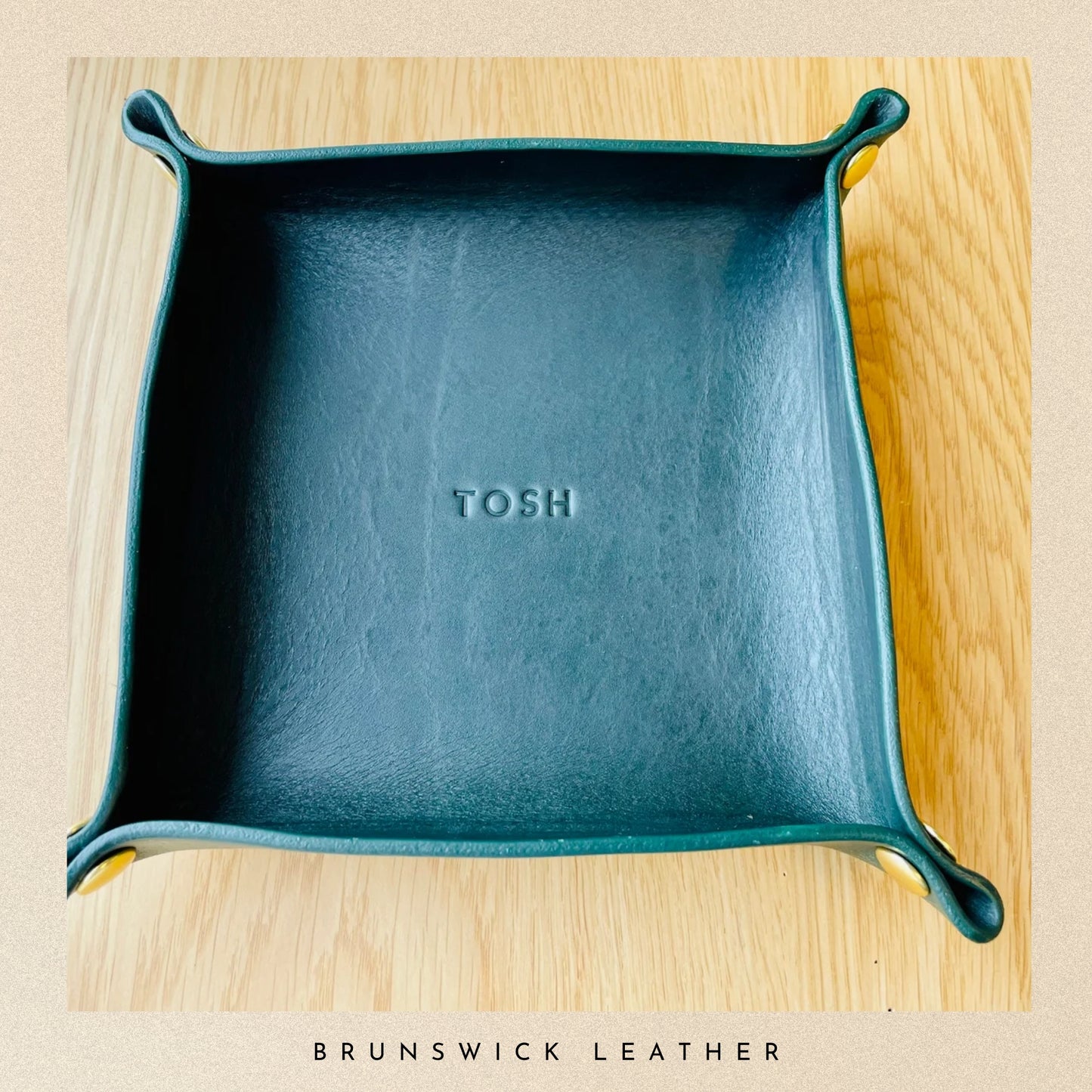 Teal leather tray with 'TOSH' branding on a wooden surface, featuring Brunswick Leather.