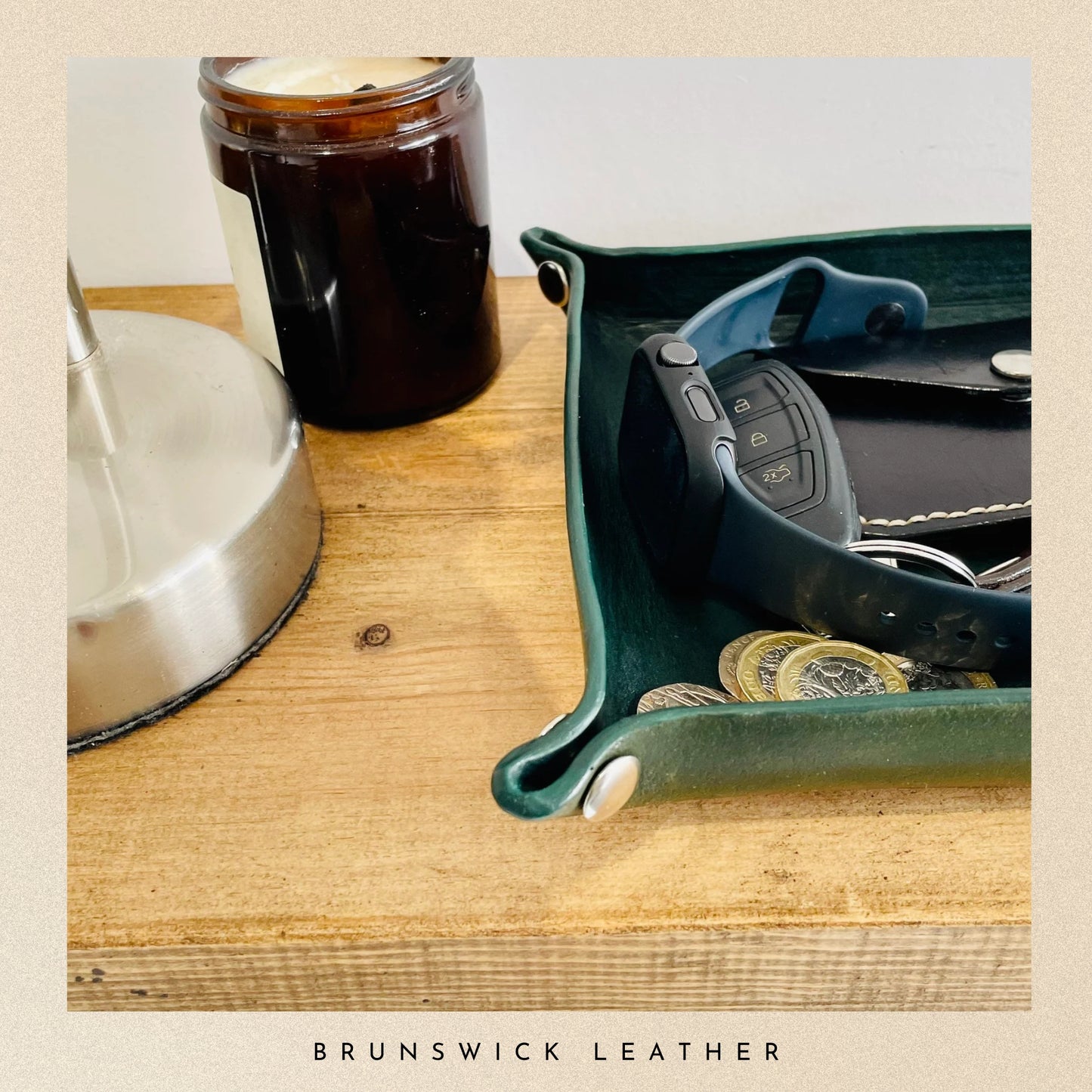 Green leather tray with car keys and coins on a wooden surface, featuring Brunswick Leather branding.