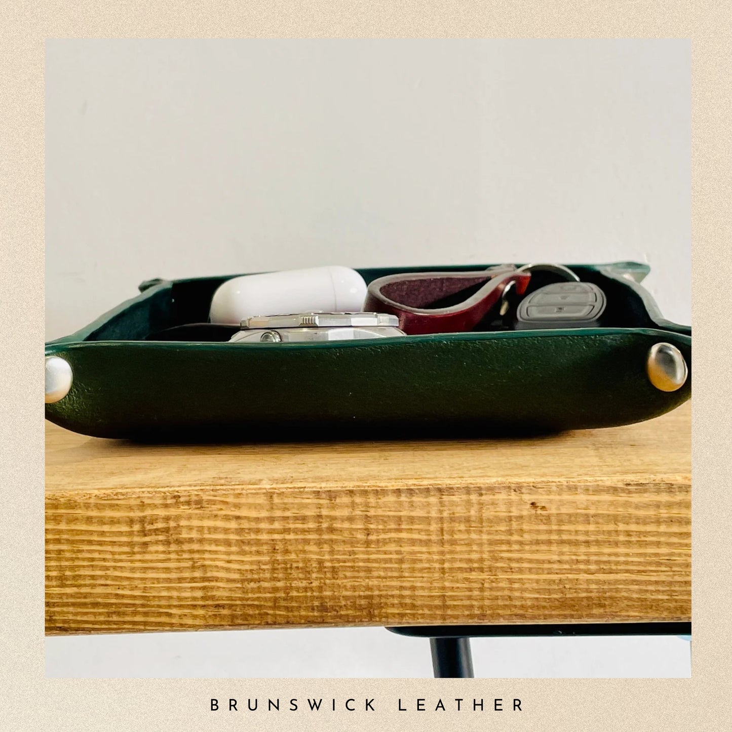 Green leather case with white and red items on a wooden surface, branded 'Brunswick Leather'.