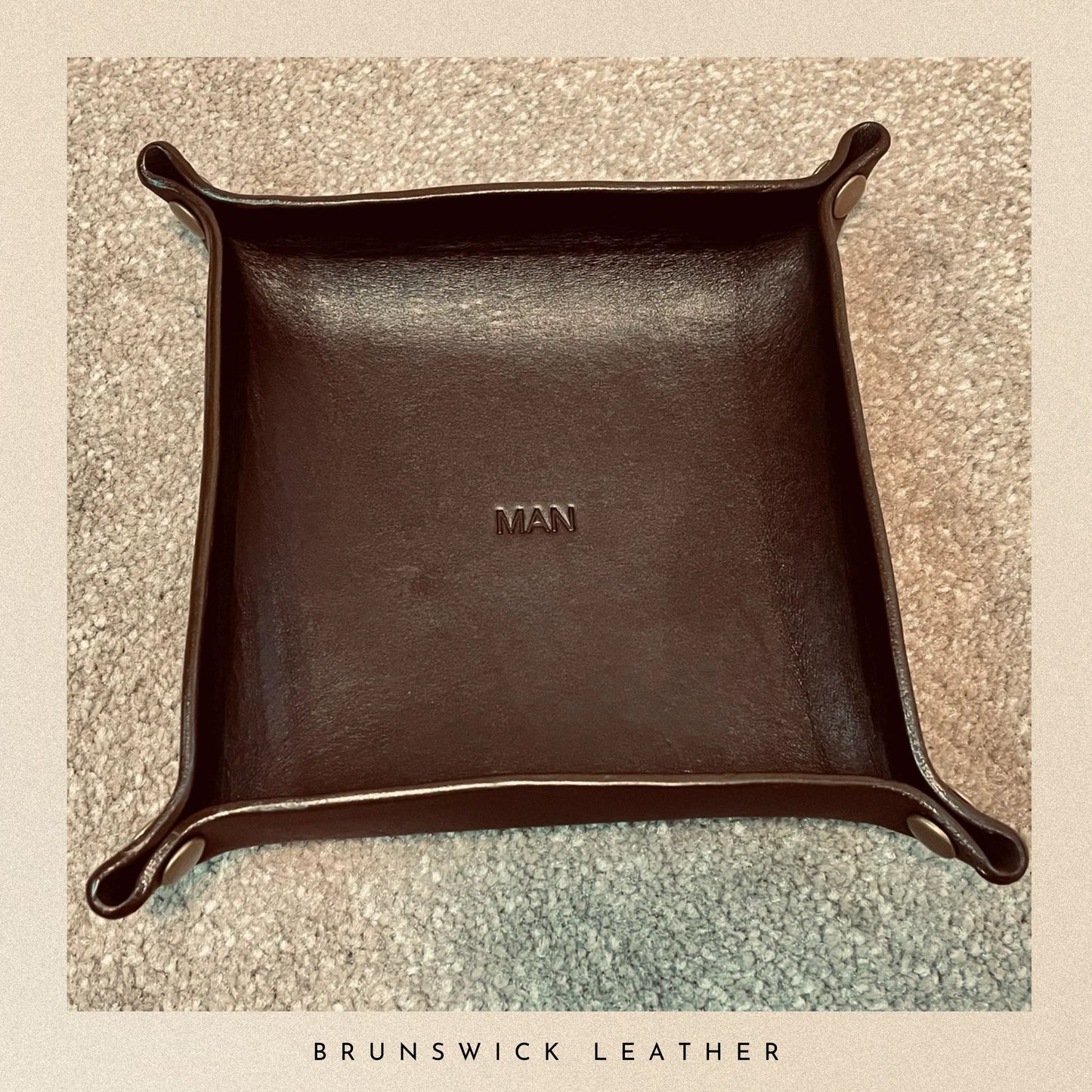 Brown leather tray with 'MAN' engraving on a textured surface, branded 'Brunswick Leather'.