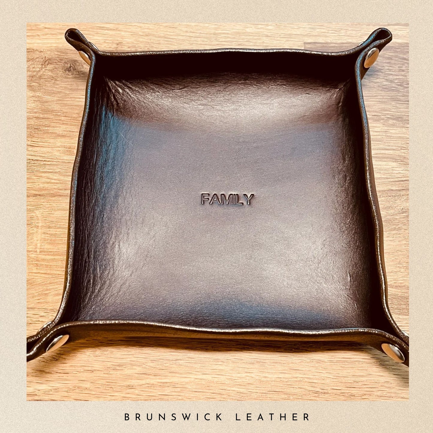 Brown leather tray with 'FAMILY' engraving on a wooden surface, branded 'Brunswick Leather'.
