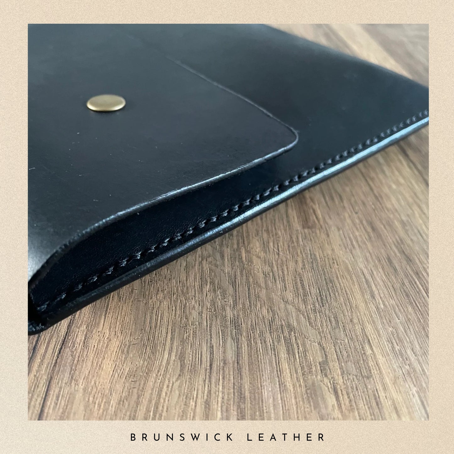 Black leather wallet with gold button on a wooden surface, branded 'Brunswick Leather'.