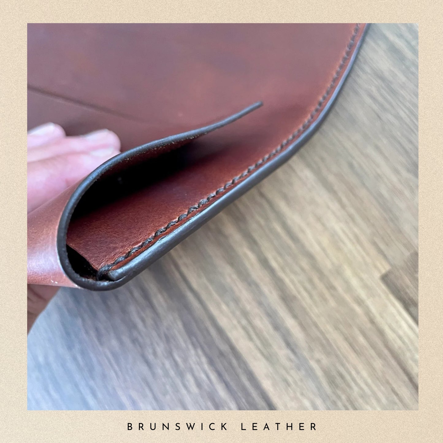 Close-up of a brown leather wallet with visible stitching on a wooden surface, branded 'Brunswick Leather'.