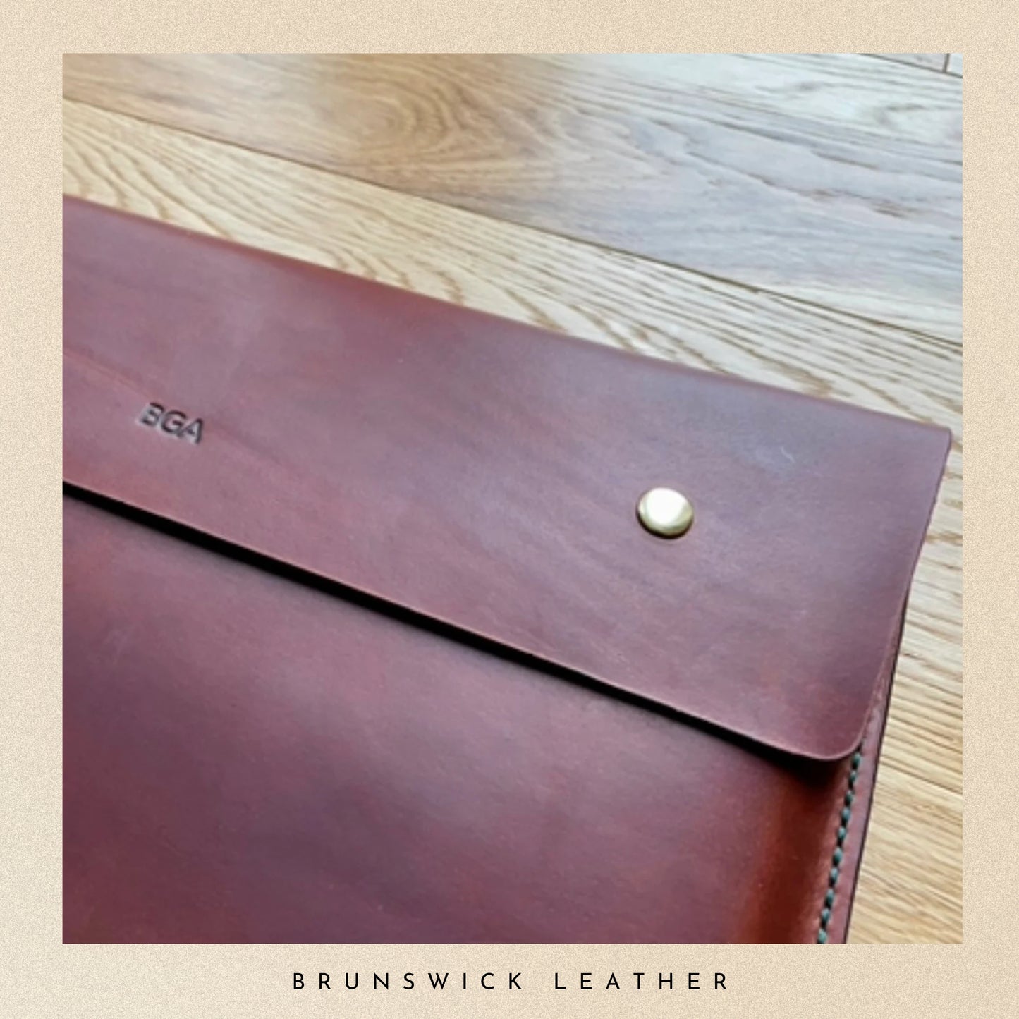 Brown leather envelope with a button closure on a wooden surface, branded 'Brunswick Leather'.