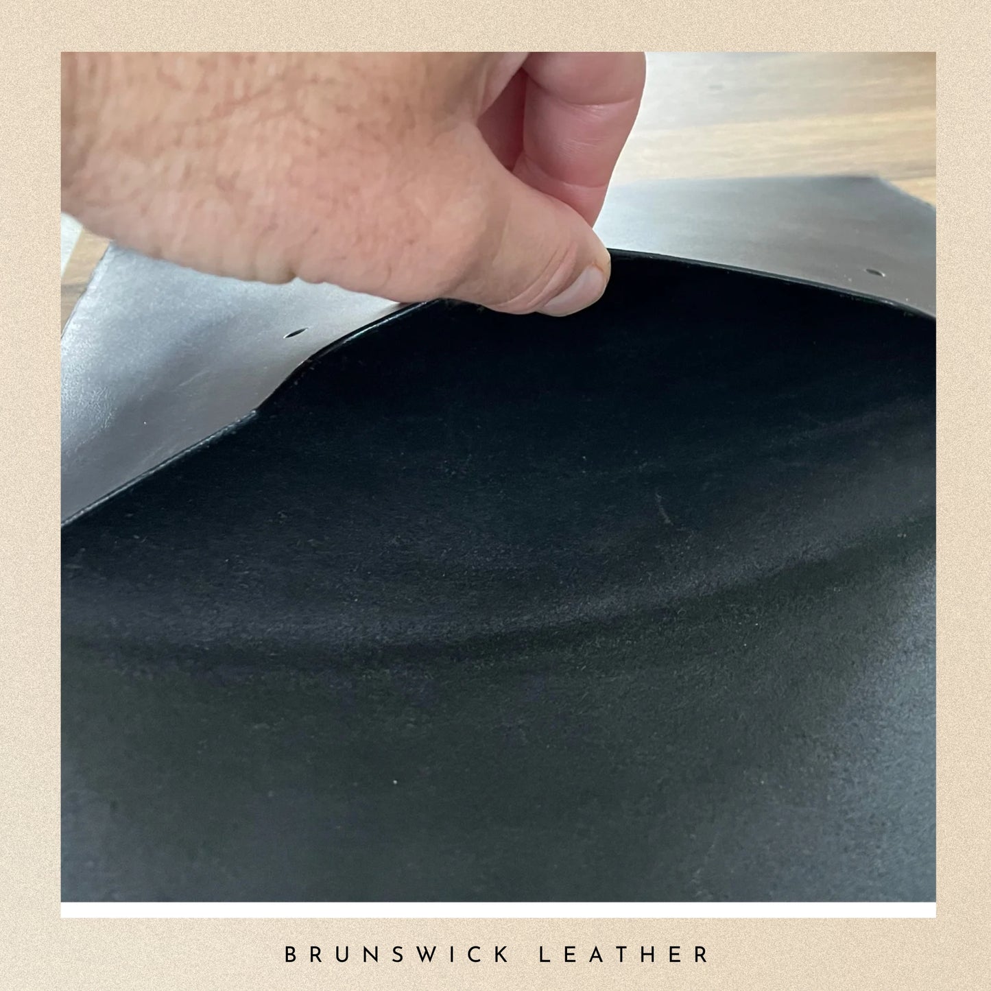 Close-up of a hand holding a piece of black leather with 'Brunswick Leather' branding.