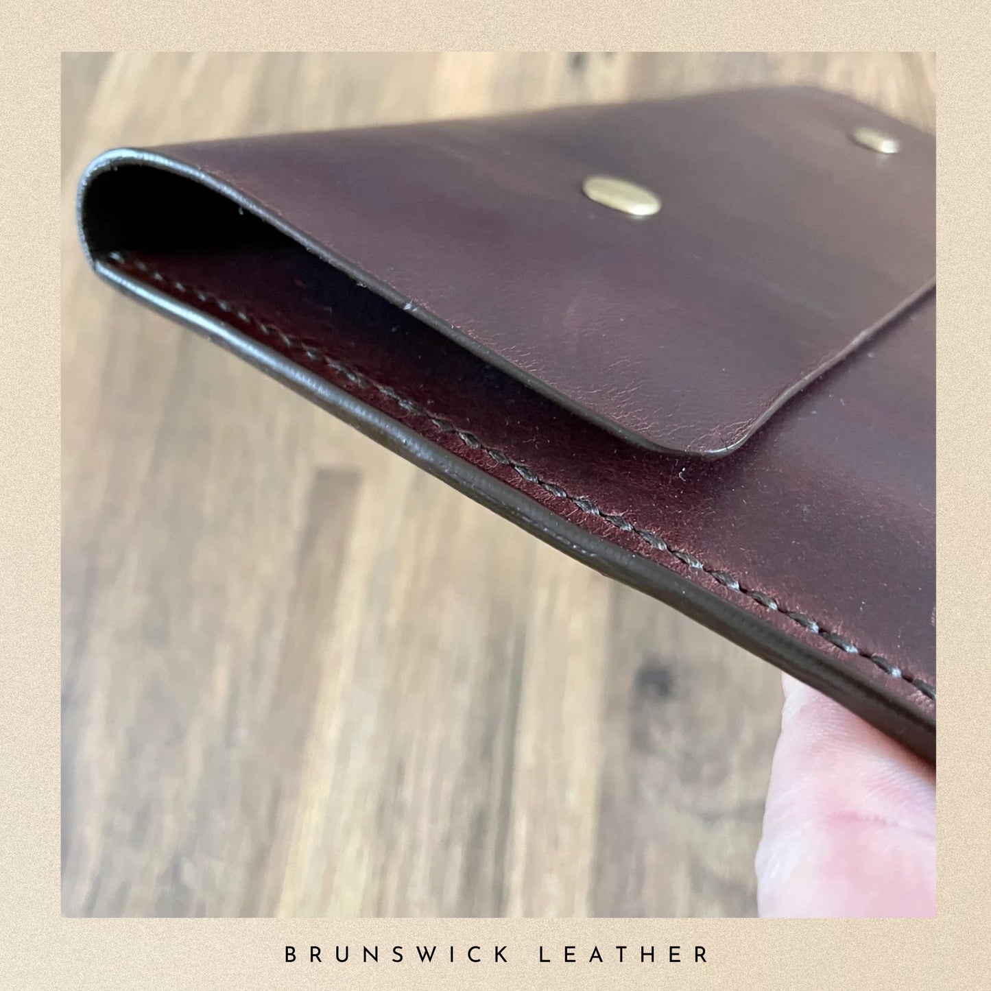 Brown leather wallet with visible stitching on a wooden surface, branded 'Brunswick Leather'.