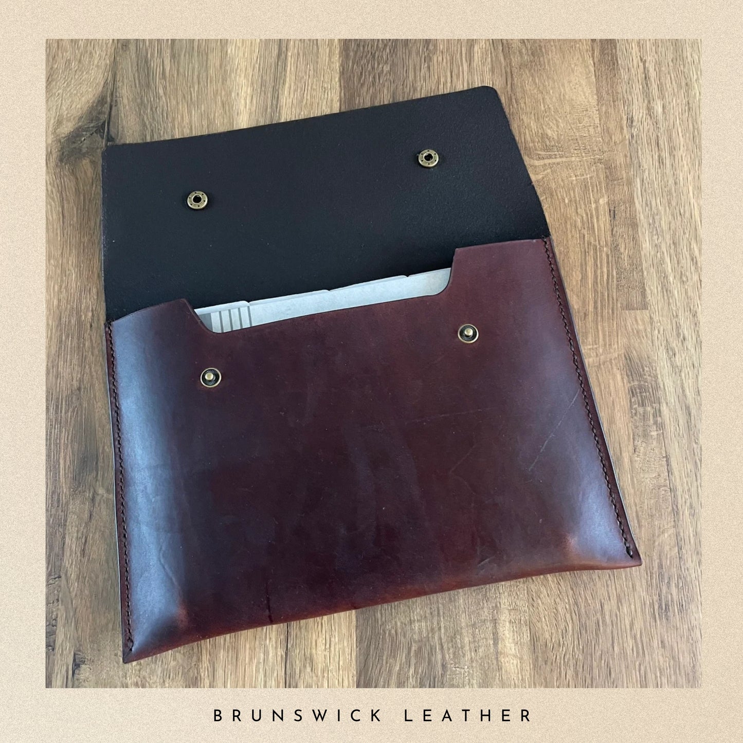 Brown leather pouch with black interior on a wooden surface, branded 'Brunswick Leather'.