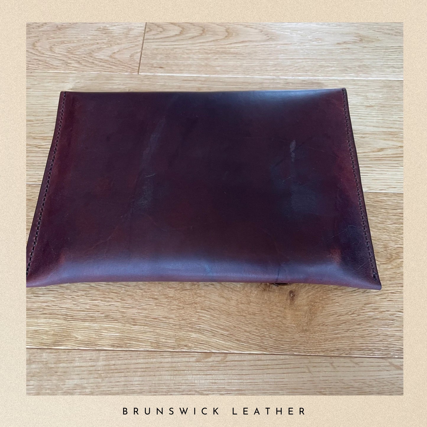 Brown leather clutch on a wooden surface with 'Brunswick Leather' branding.