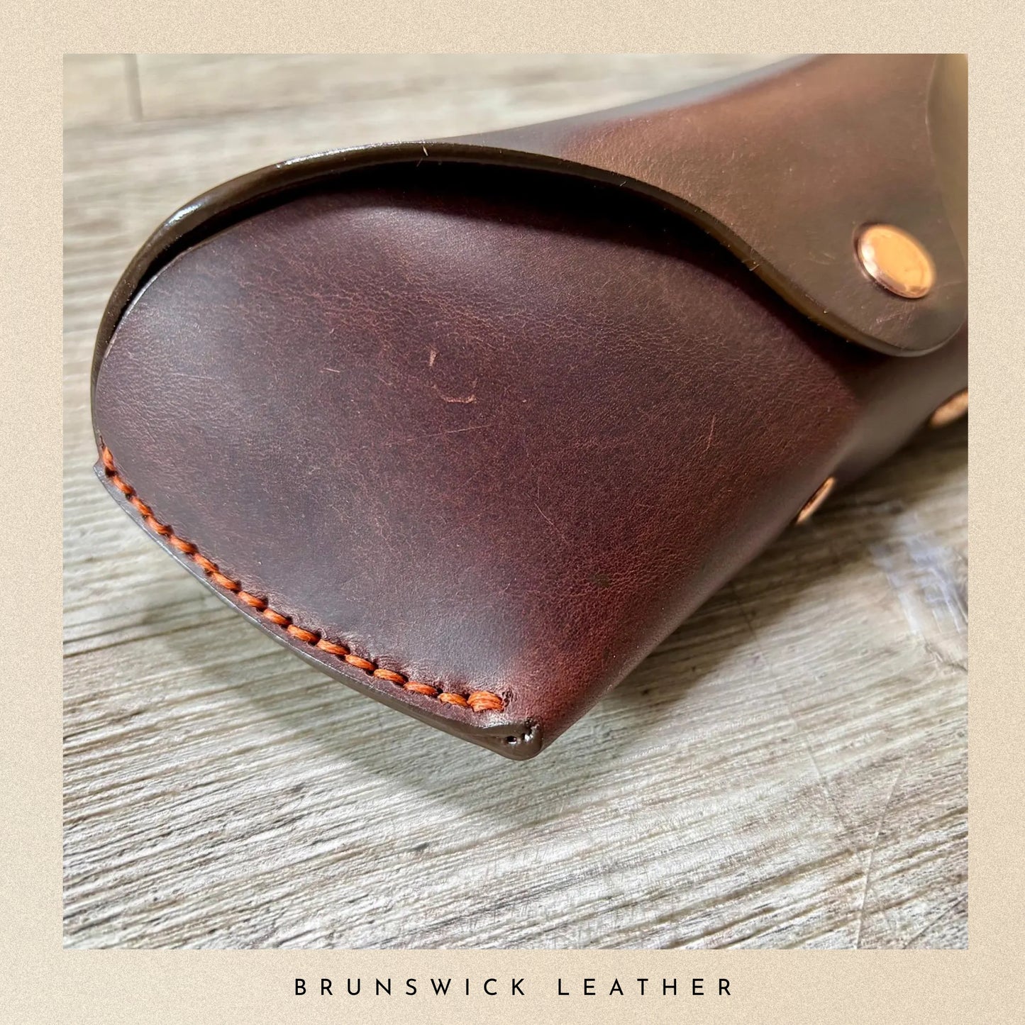 Brown leather case with visible stitching on a wooden surface, branded 'Brunswick Leather'.
