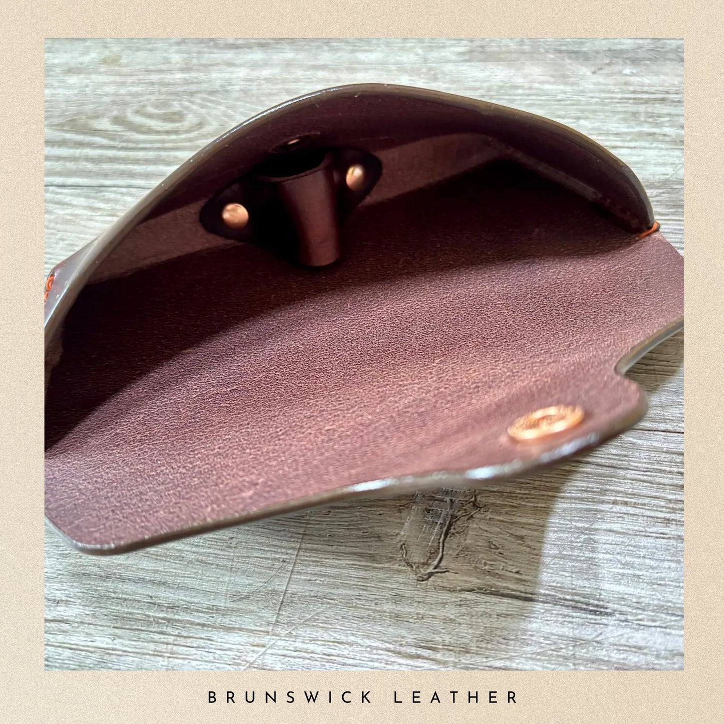 Brown leather wallet with gold accents on a wooden surface, branded 'Brunswick Leather'.