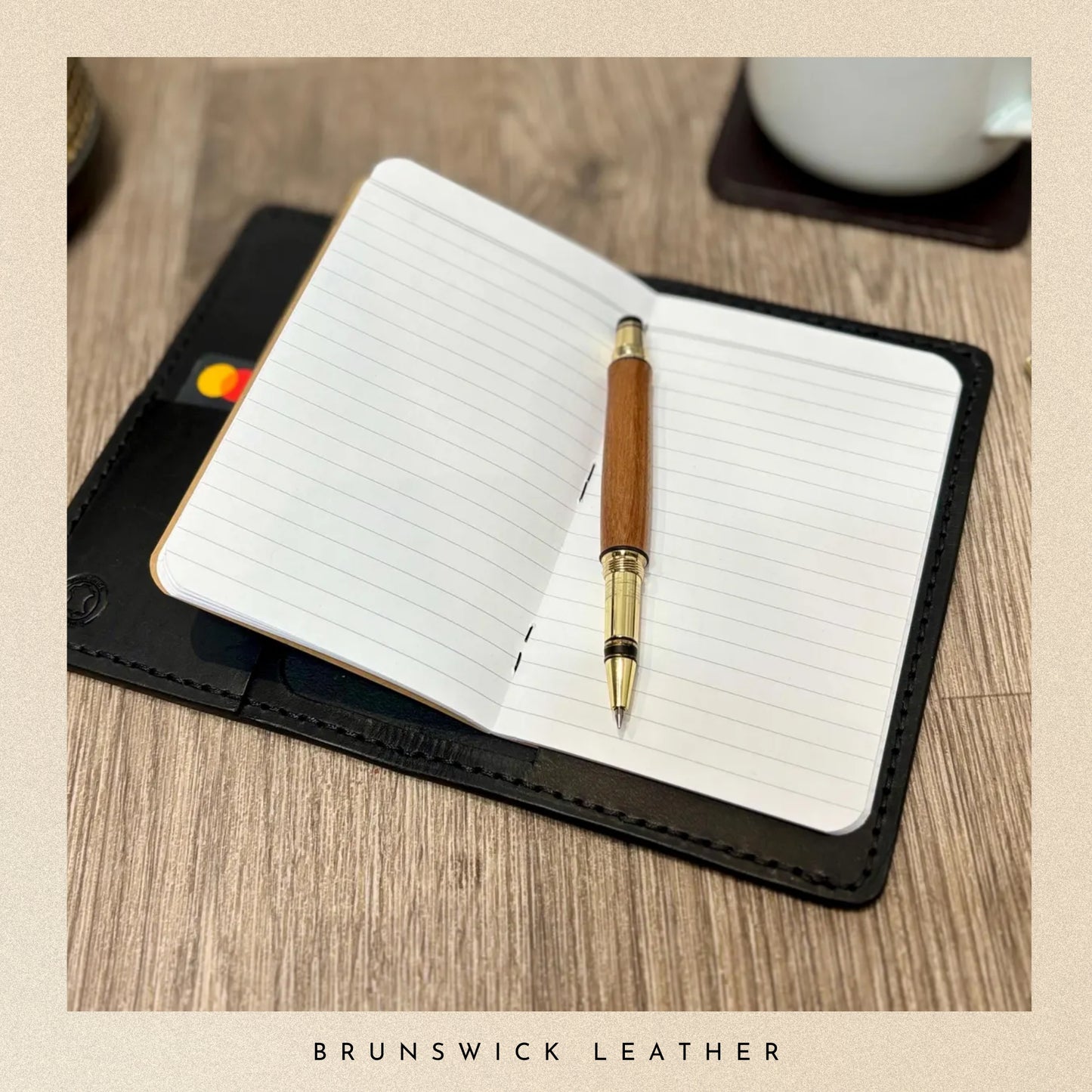 Open notebook with a pen on a wooden surface, featuring Brunswick Leather branding.