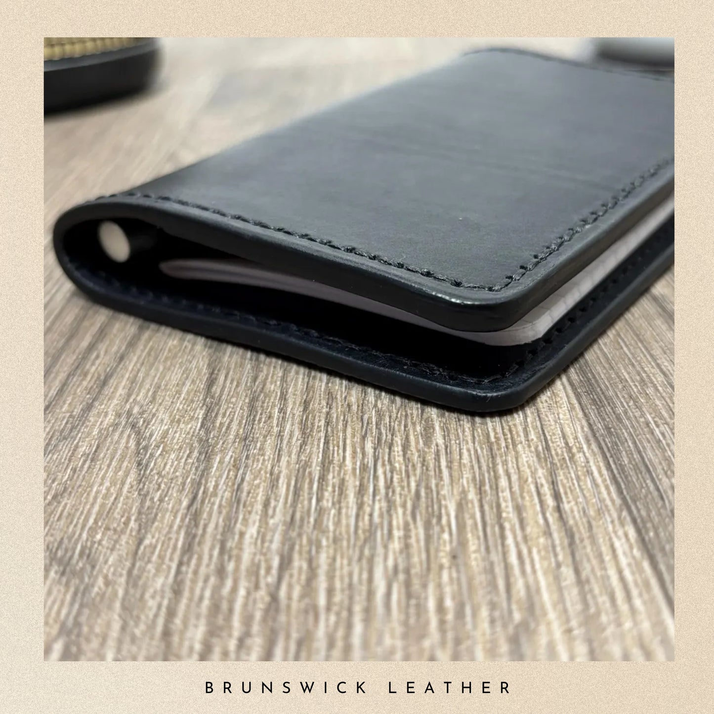 Black leather wallet on a wooden surface with 'Brunswick Leather' branding.