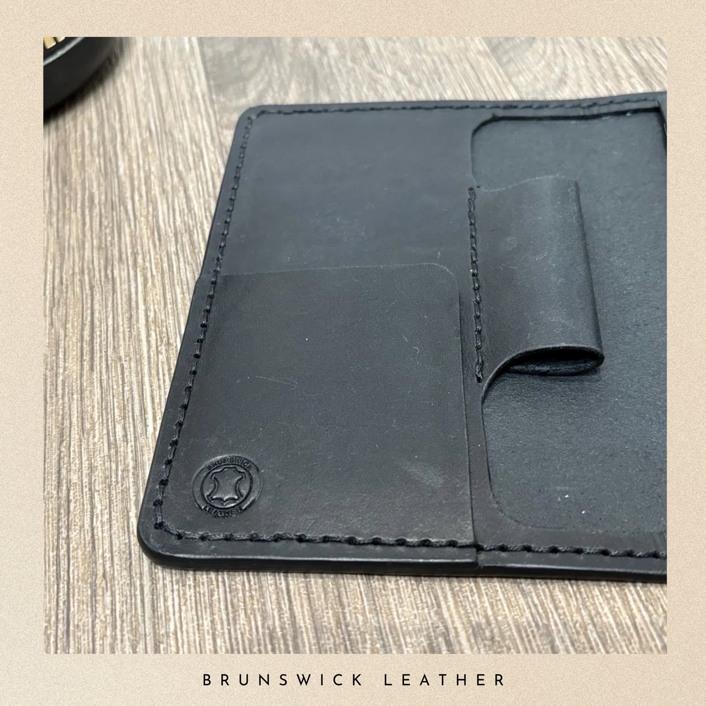 Black leather wallet with visible stitching on a wooden surface, branded 'Brunswick Leather'.