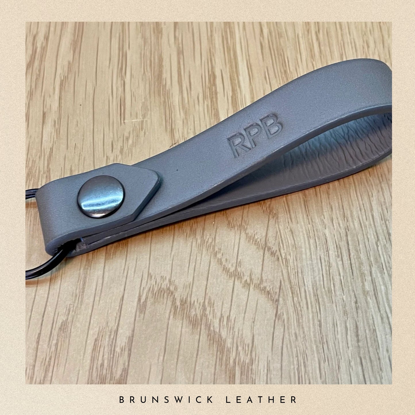 Grey leather strap with 'RPB' branding on a wooden surface, featuring 'Brunswick Leather' text.