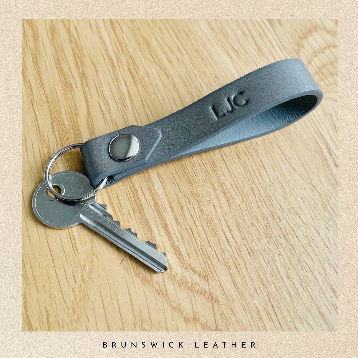 Gray leather keychain with keys on a wooden surface, branded 'LJC'.