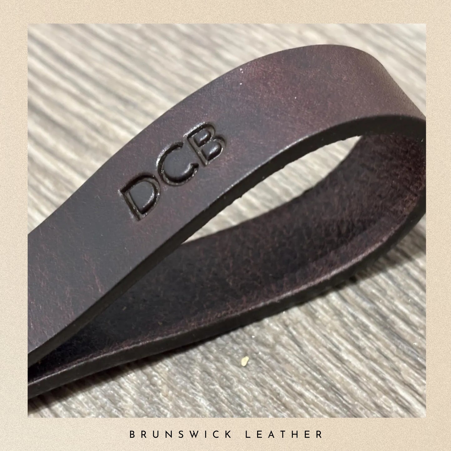 Brown leather strap with 'DCB' engraving on a textured surface, branded 'Brunswick Leather'.