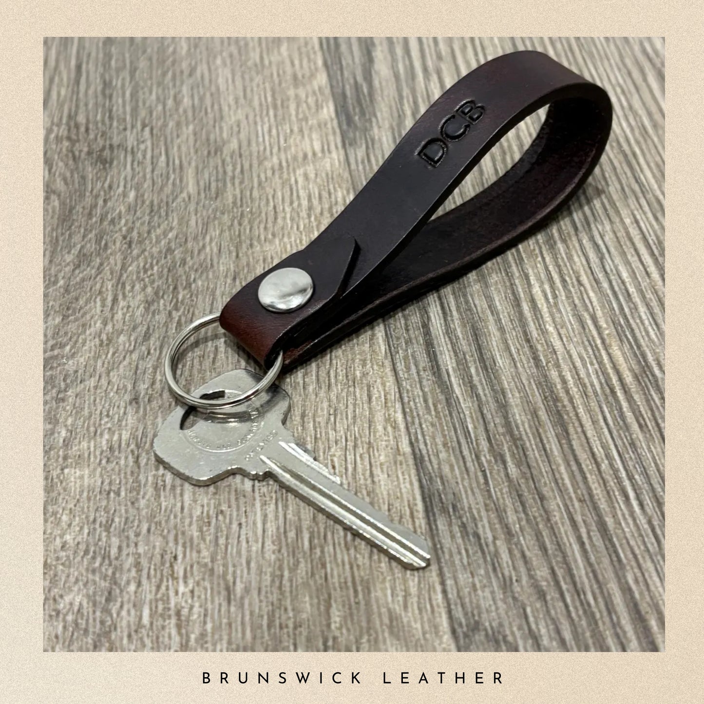 Brown leather keychain with silver key on a wooden surface, branded 'Brunswick Leather'.