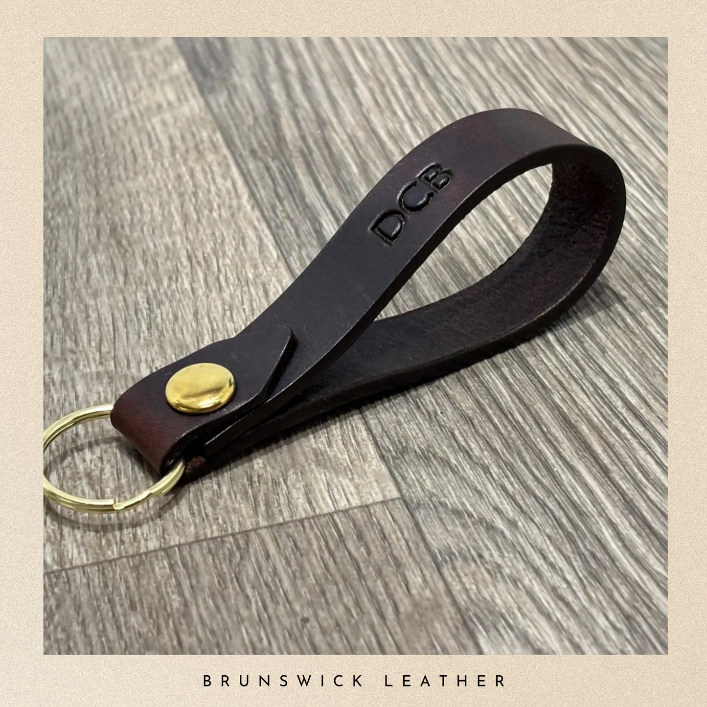 Brown leather keychain with gold accent on a wooden surface, branded 'DCB'.