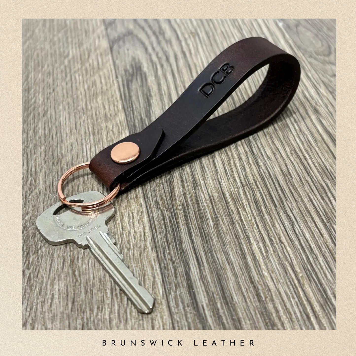 Brown leather keychain with a key on a wooden surface, branded 'Brunswick Leather'.
