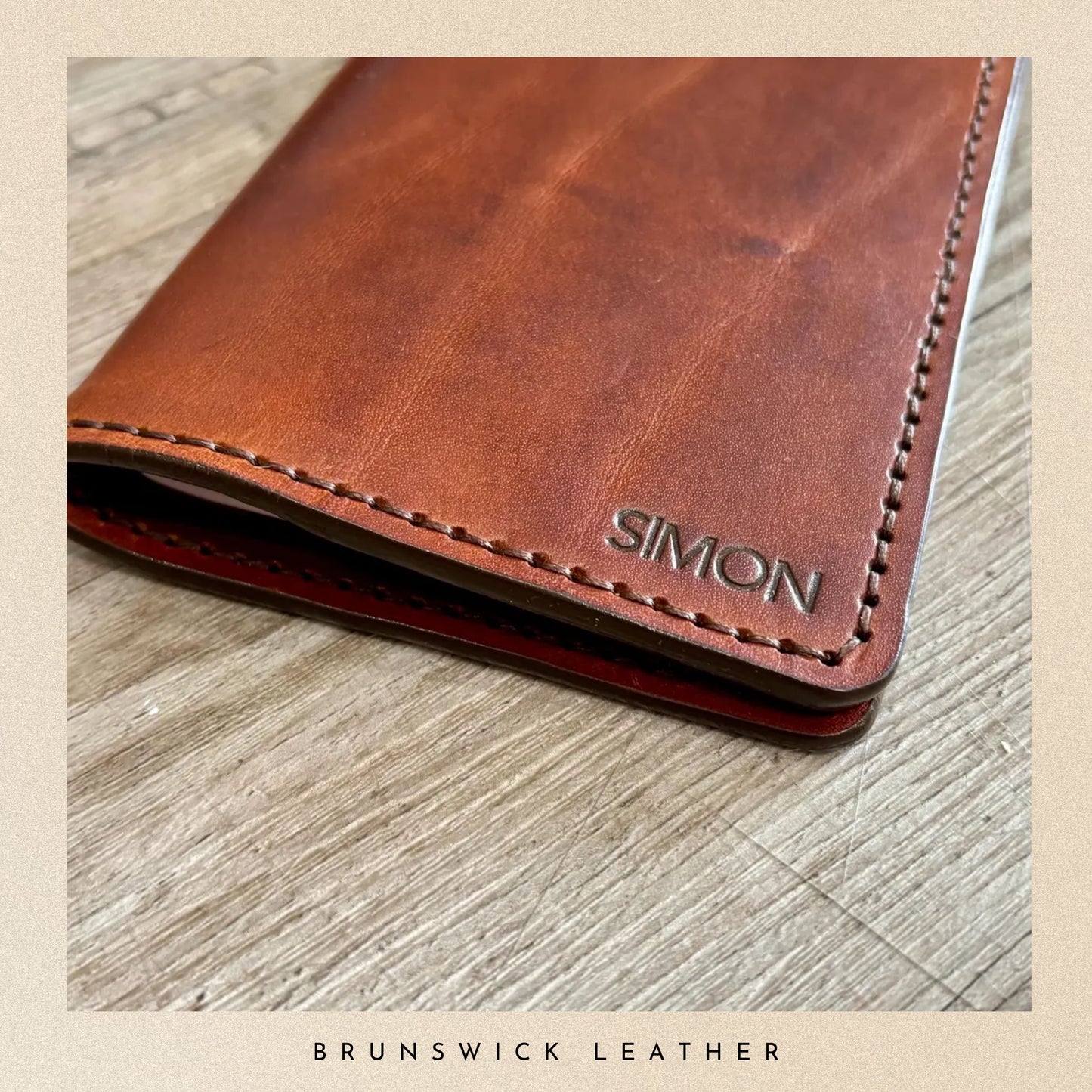 Brown leather wallet with 'SIMON' branding on a wooden surface, featuring Brunswick Leather text.