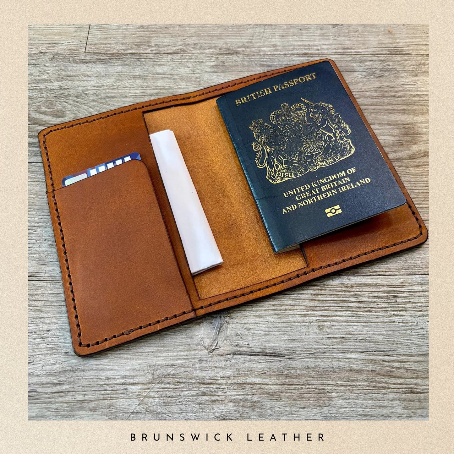 Brown leather passport holder with a British passport on a wooden surface, branded 'Brunswick Leather'.