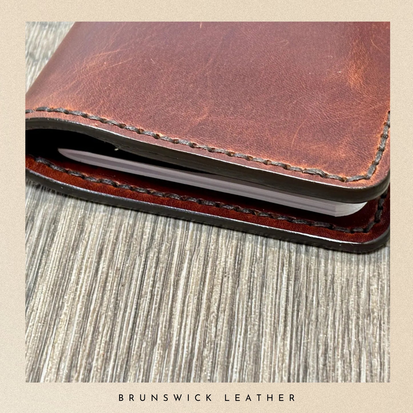 Brown leather wallet with visible stitching on a textured surface, branded 'Brunswick Leather'.