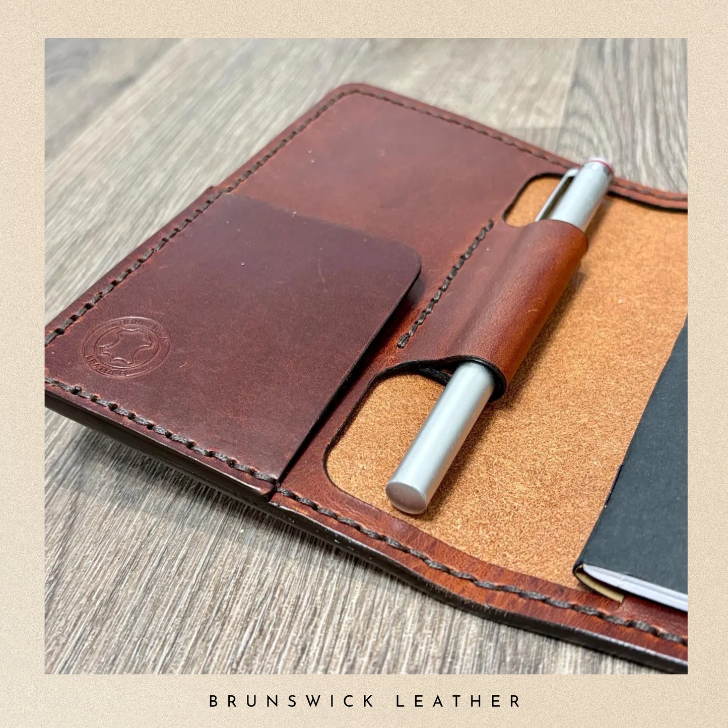 Brown leather notebook with pen holder on a wooden surface, featuring 'Brunswick Leather' branding.