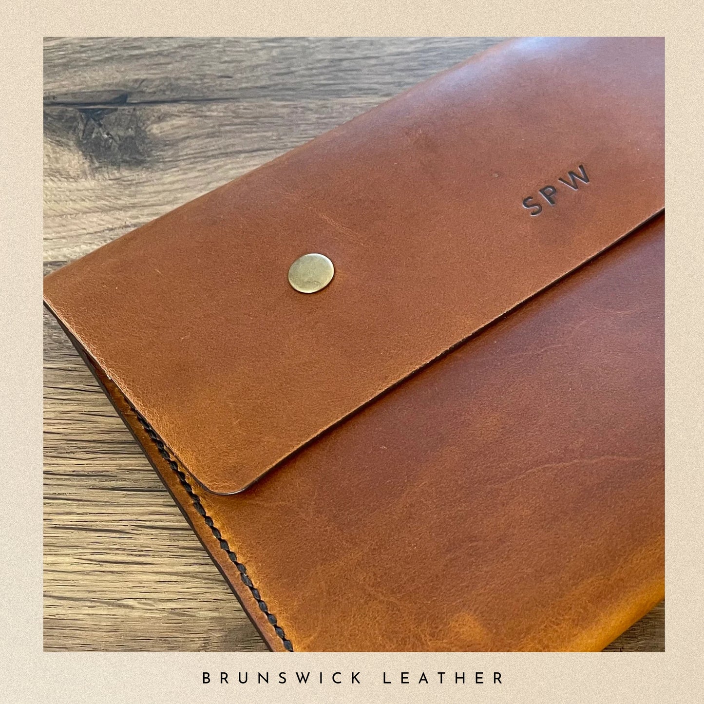 Brown leather wallet with 'SPW' initials on a wooden surface, branded 'Brunswick Leather'.