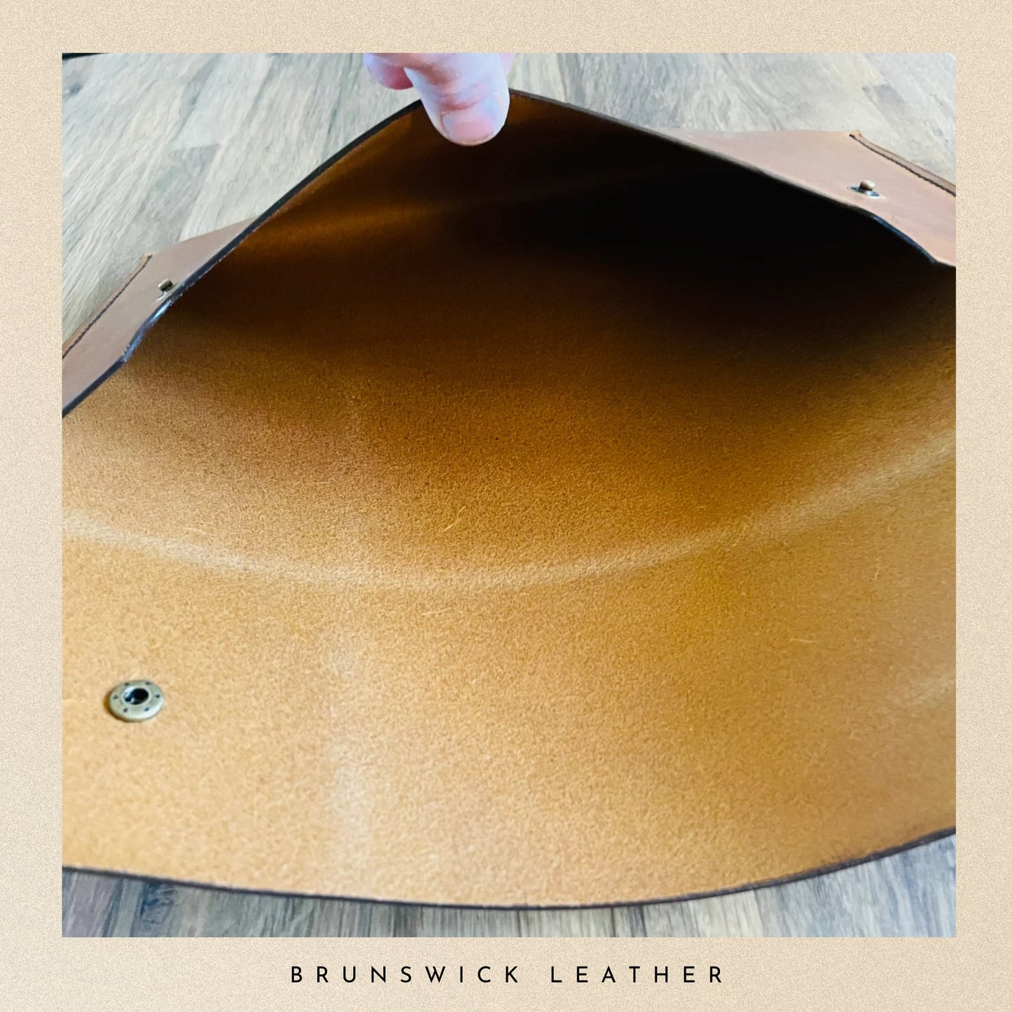 Close-up of a brown leather surface with a hand holding it, on a wooden floor.