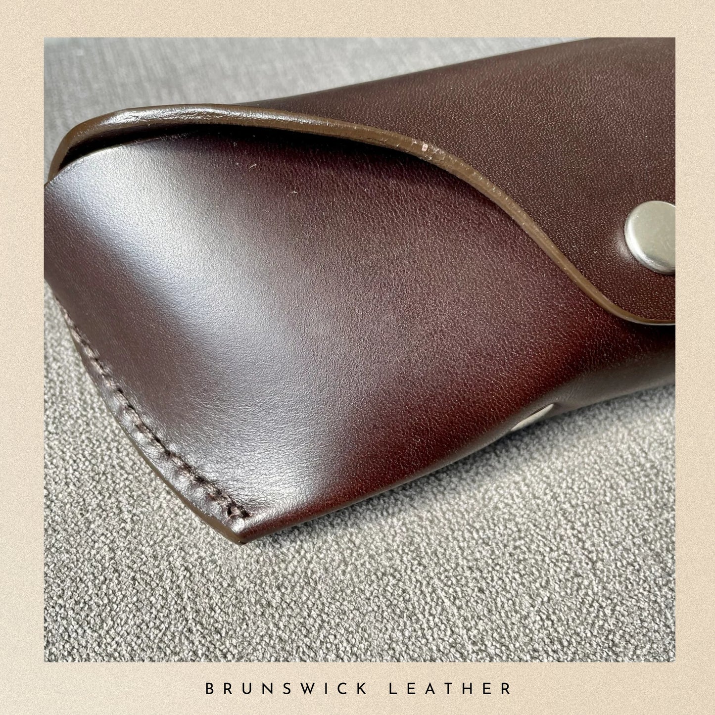 Close-up of a brown leather product with visible stitching on a textured beige surface, branded 'Brunswick Leather'.