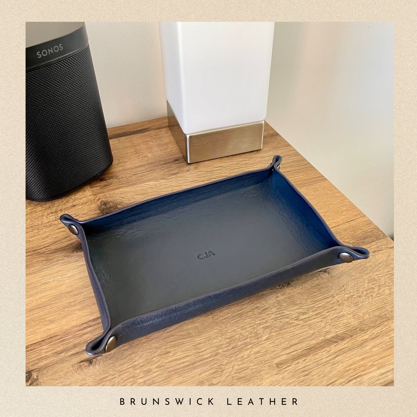 Blue leather tray on a wooden surface with a black speaker and white cube in the background.