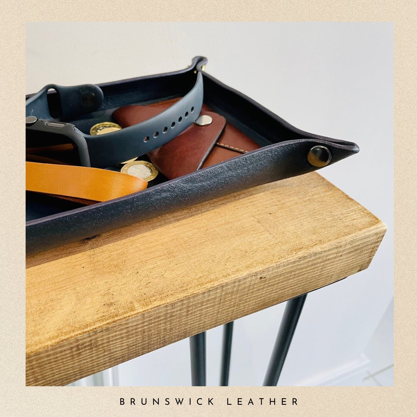 Tray with leather belts on a wooden surface, featuring the brand 'Brunswick Leather'.