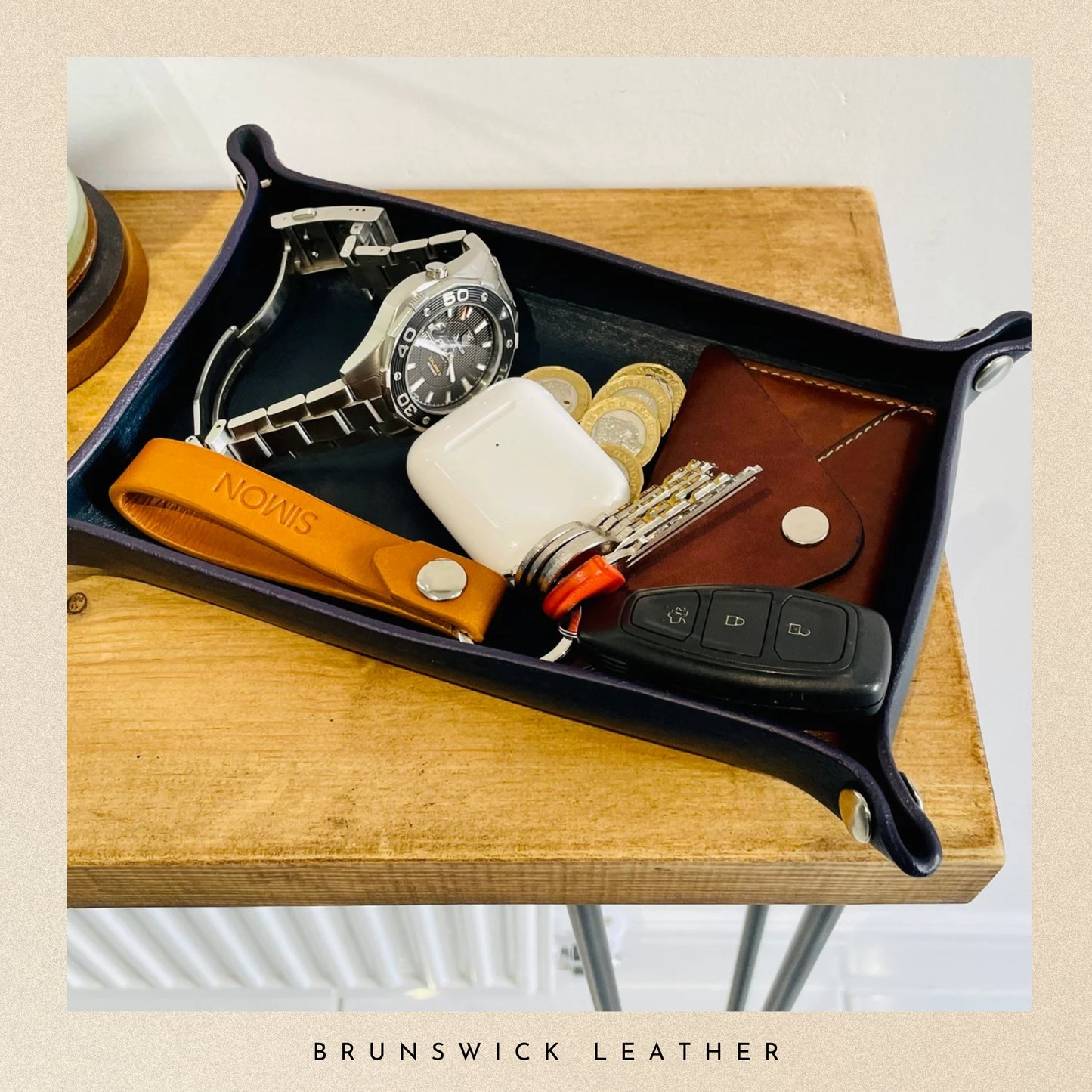 Tray with assorted items including a watch, keys, and phone case on a wooden surface with 'Brunswick Leather' branding.