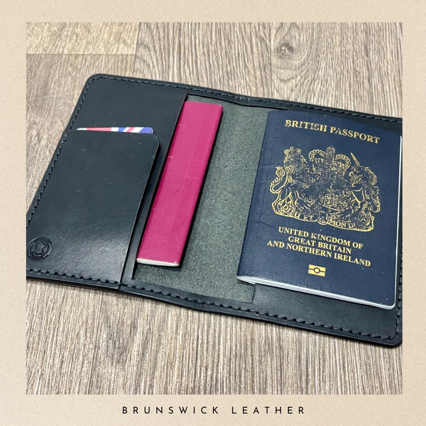 Black leather passport holder with a British passport and pink card on a wooden surface, branded 'Brunswick Leather'.