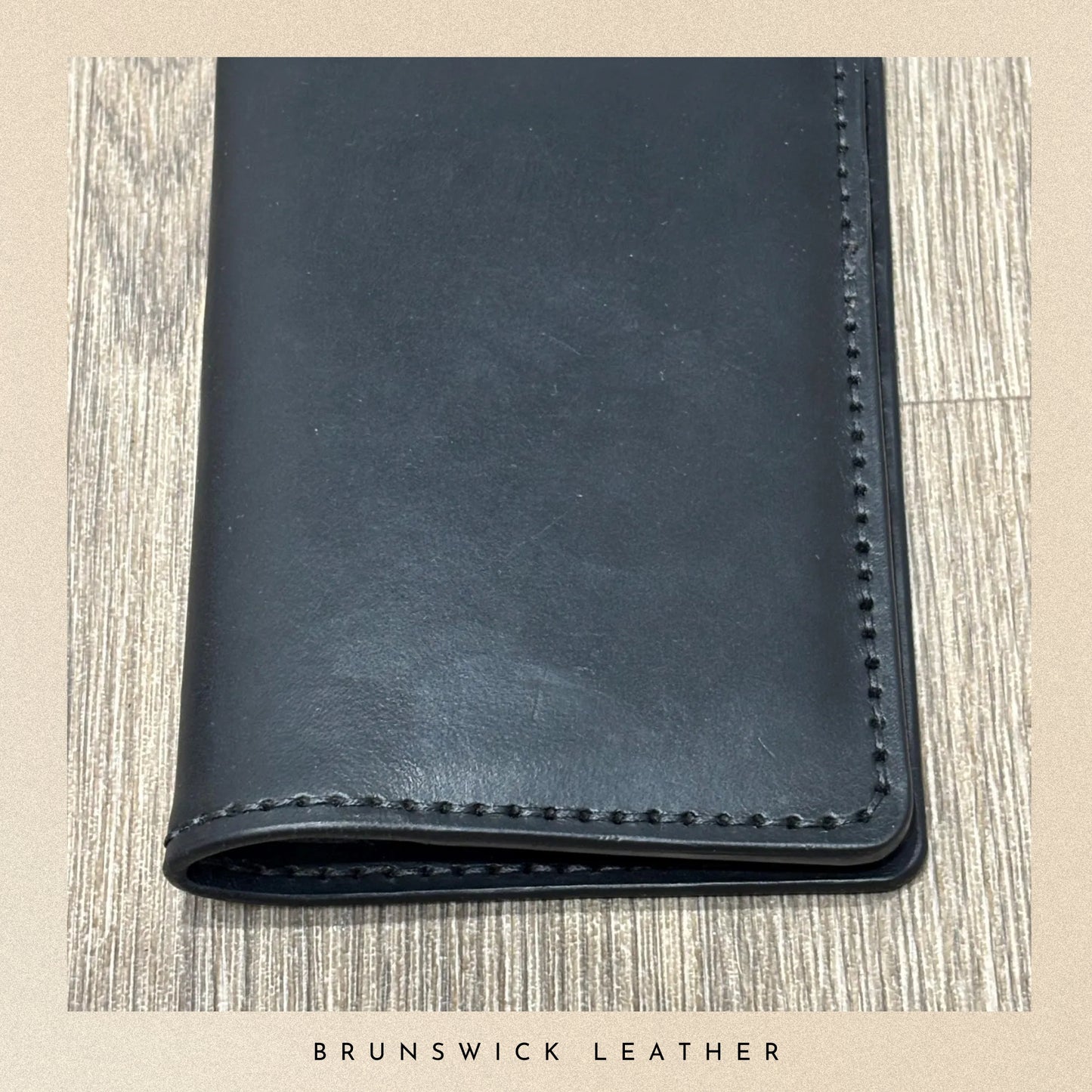 Black leather wallet on a wooden surface with 'Brunswick Leather' branding.