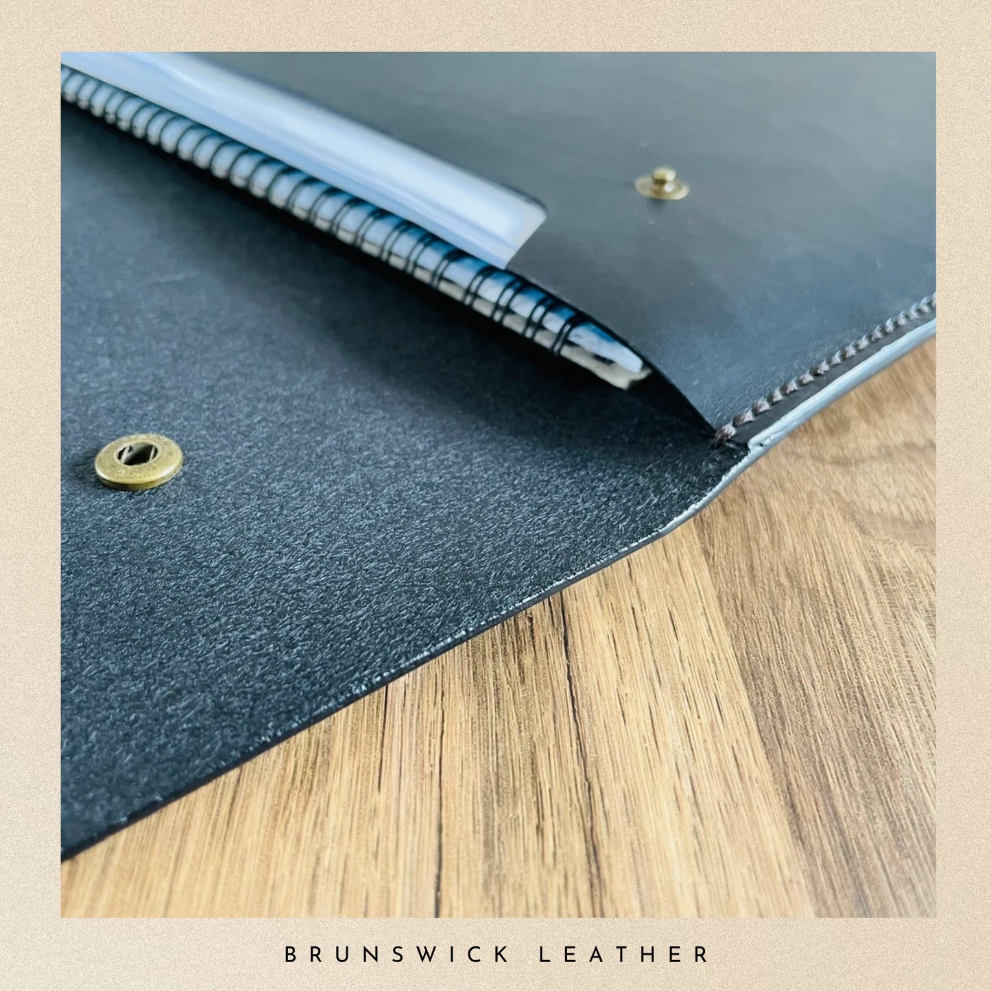Blue leather notebook cover with gold rivets on a wooden surface, branded 'Brunswick Leather'.