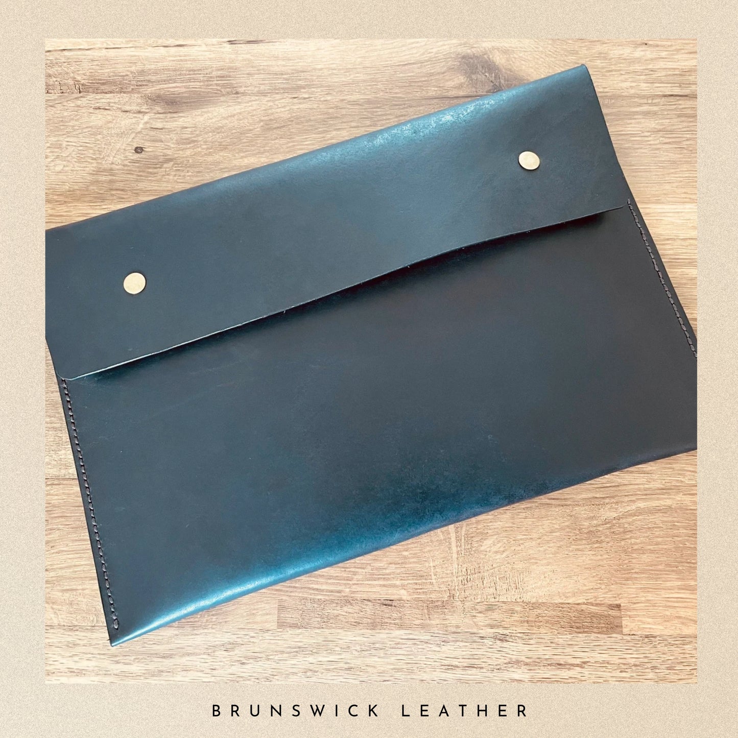 Blue leather envelope on a wooden surface with 'Brunswick Leather' branding.