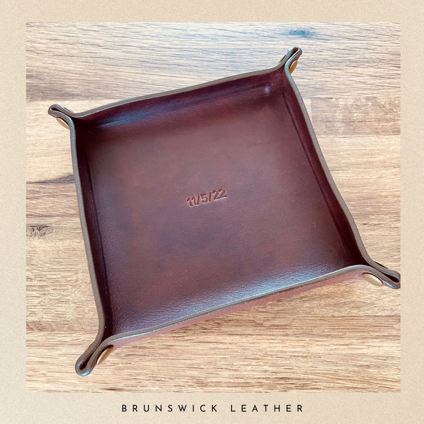Brown leather tray with 'Kubek' branding on a wooden surface, featuring 'Brunswick Leather' branding at the bottom.