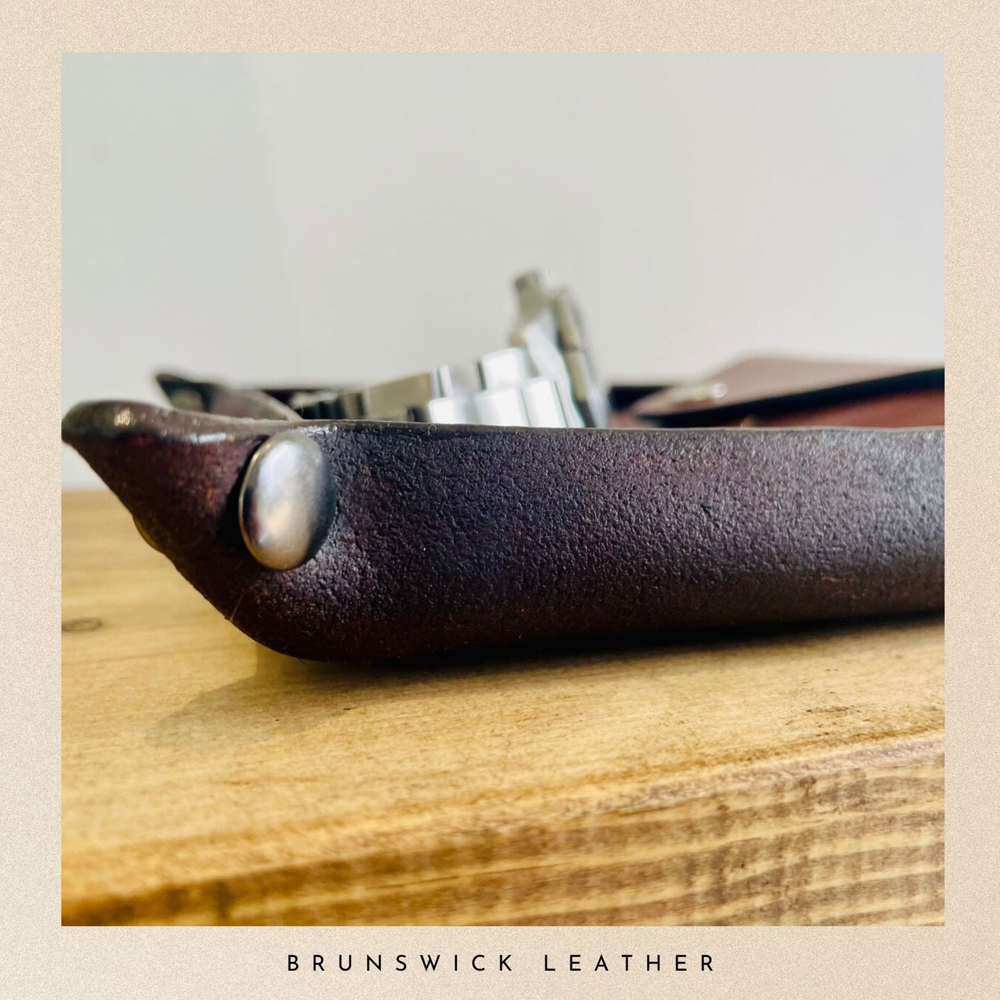 Close-up of a leather product with metallic accents on a wooden surface, branded 'Brunswick Leather'.