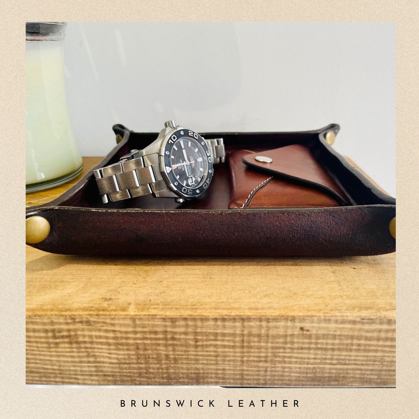 Leather tray with a watch and wallet on a wooden surface, branded 'Brunswick Leather'.