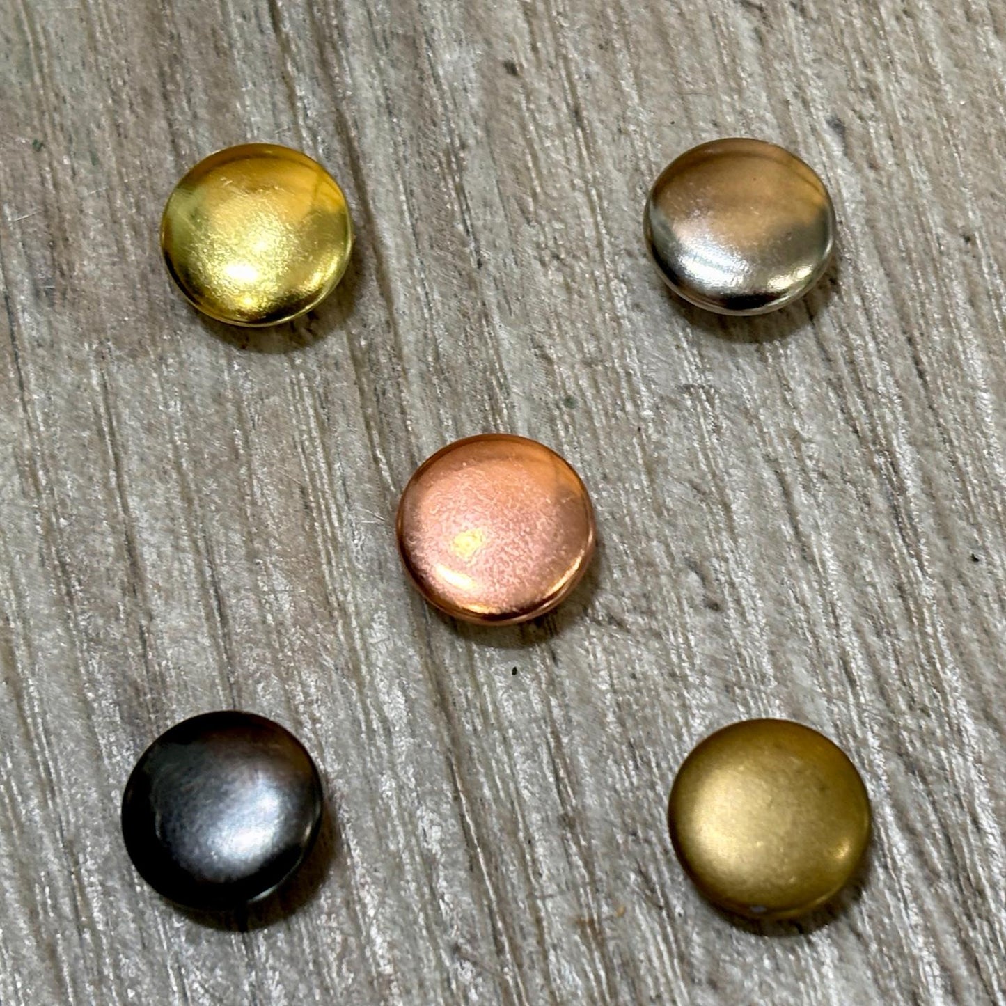 Five metallic buttons in gold, bronze, and black on a wooden surface