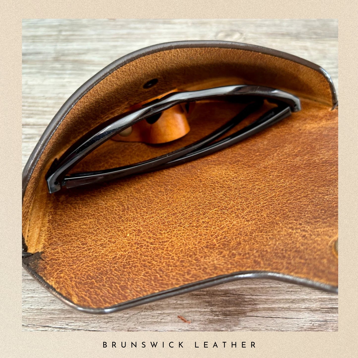 Brown leather saddle with metal hardware on a wooden background, branded 'Brunswick Leather'.