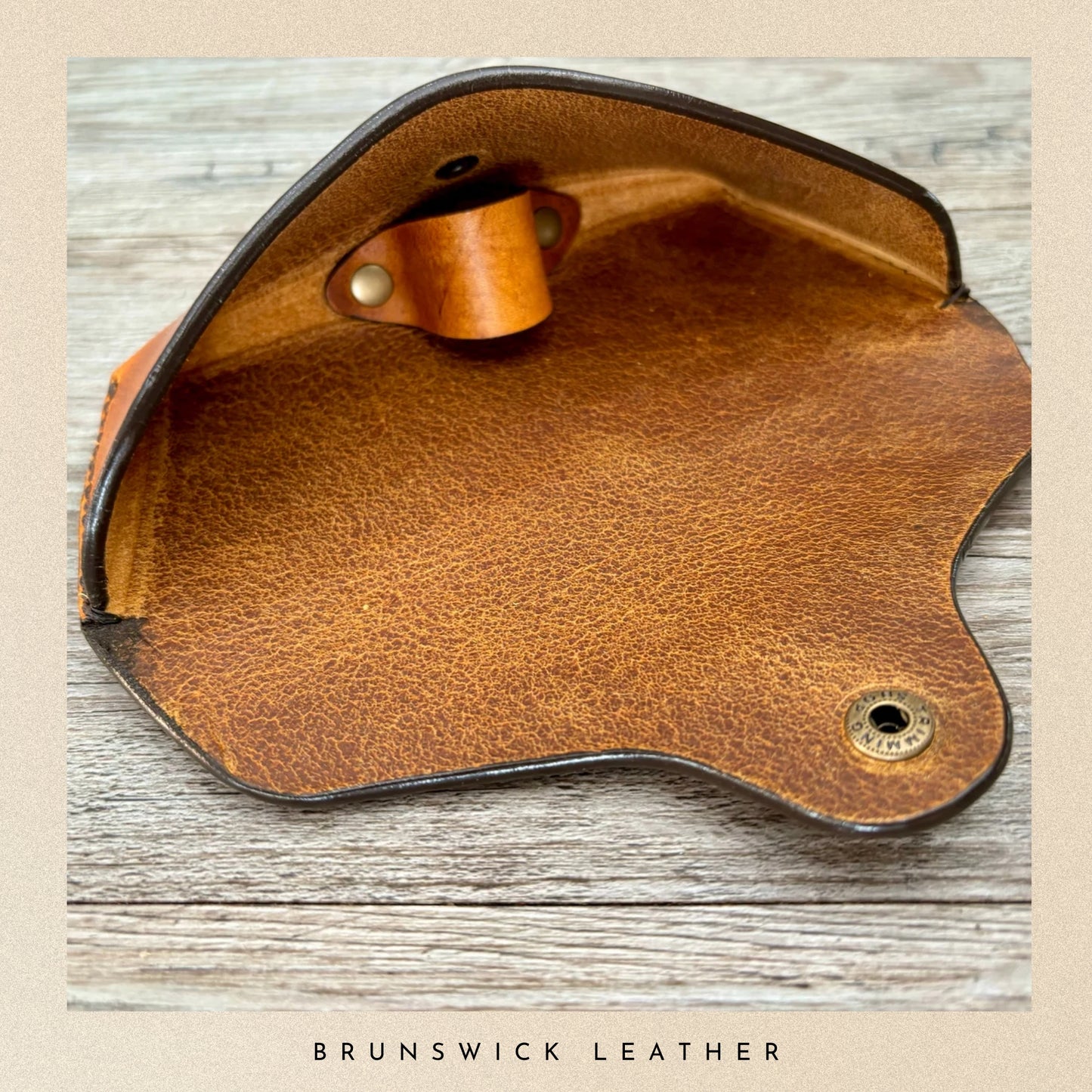 Brown leather product with gold accents on a wooden surface, branded 'Brunswick Leather'.