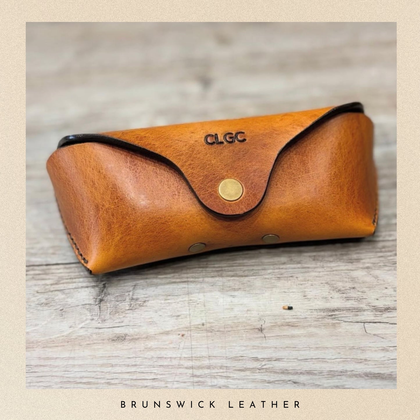 Brown leather glasses case with gold clasp on a wooden surface, branded 'CLGC'.