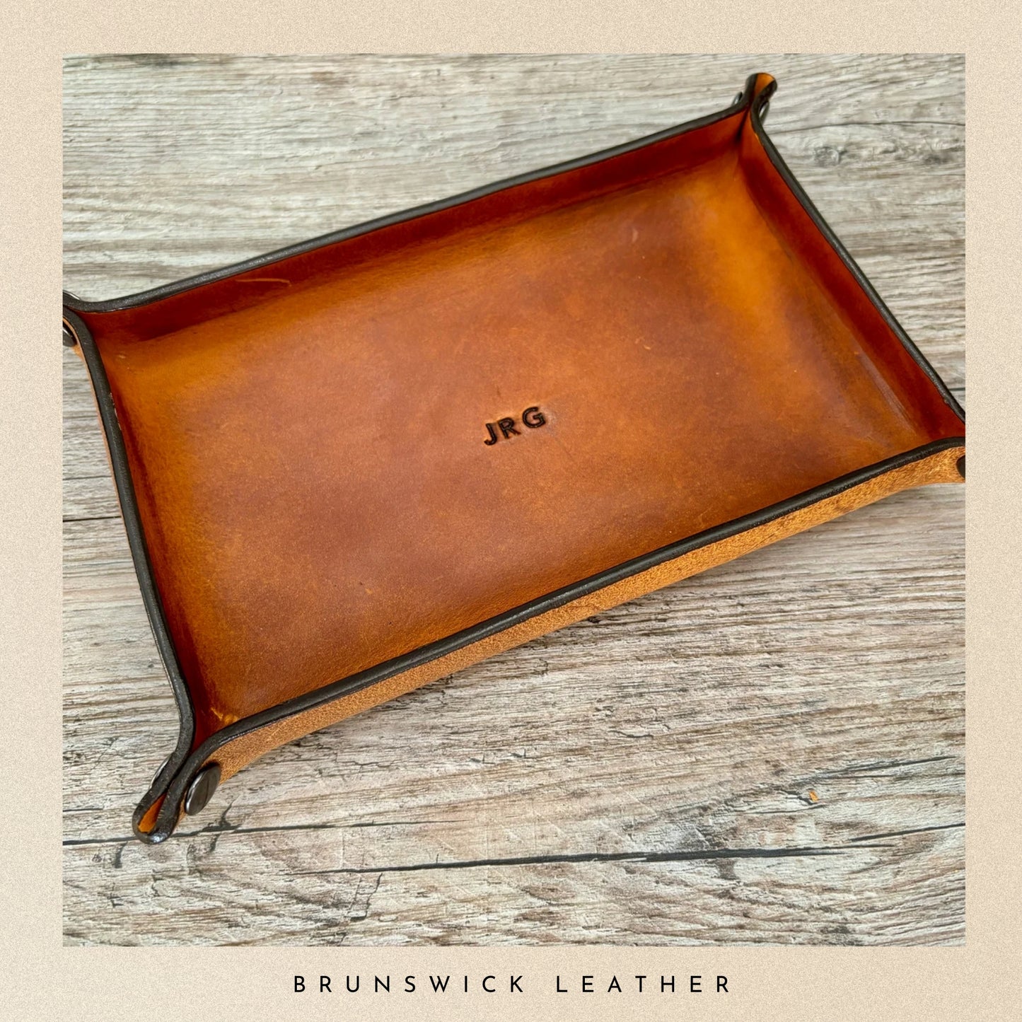 Brown leather tray with 'JRG' engraving on a wooden surface, branded 'Brunswick Leather'.