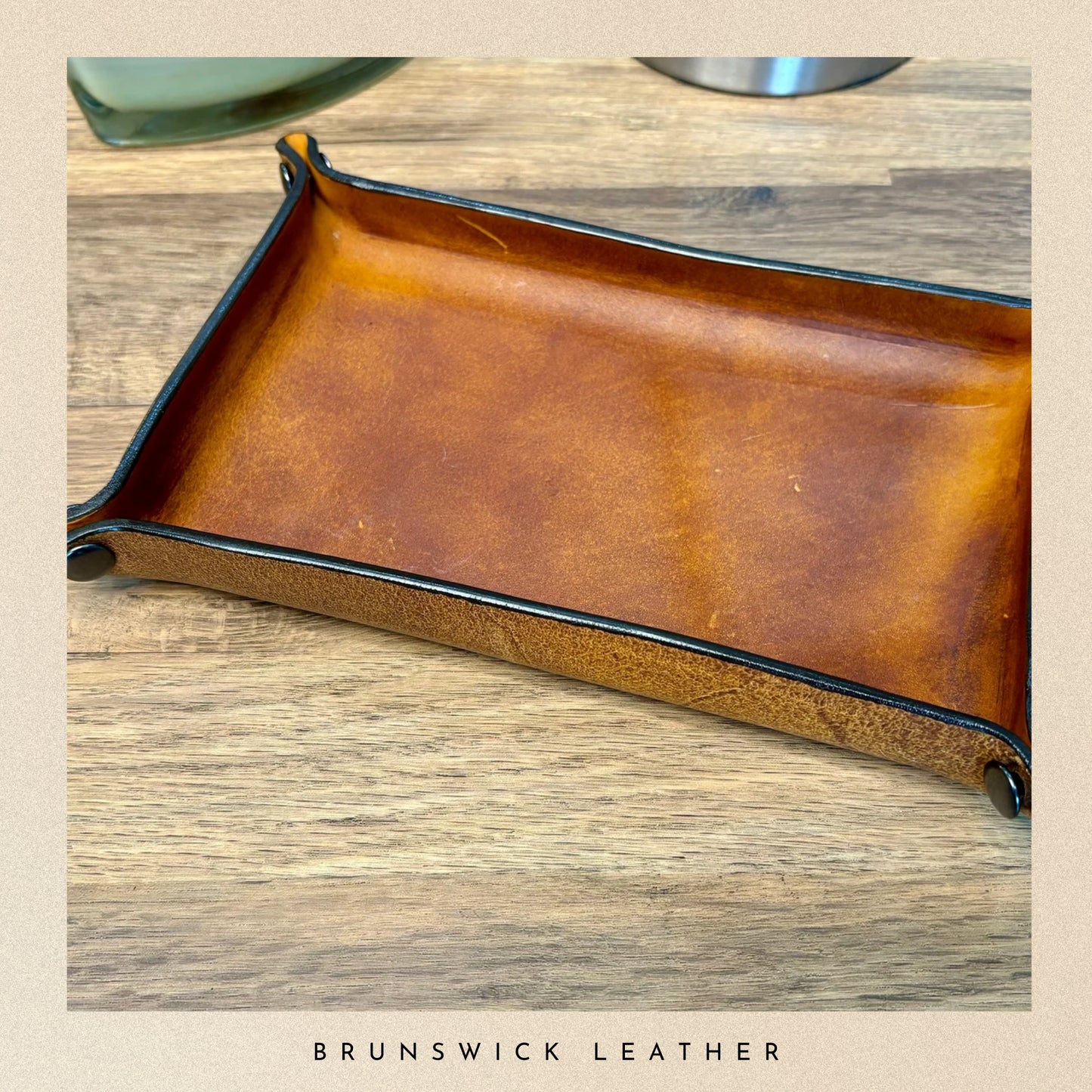Brown leather tray on a wooden surface with 'Brunswick Leather' branding.
