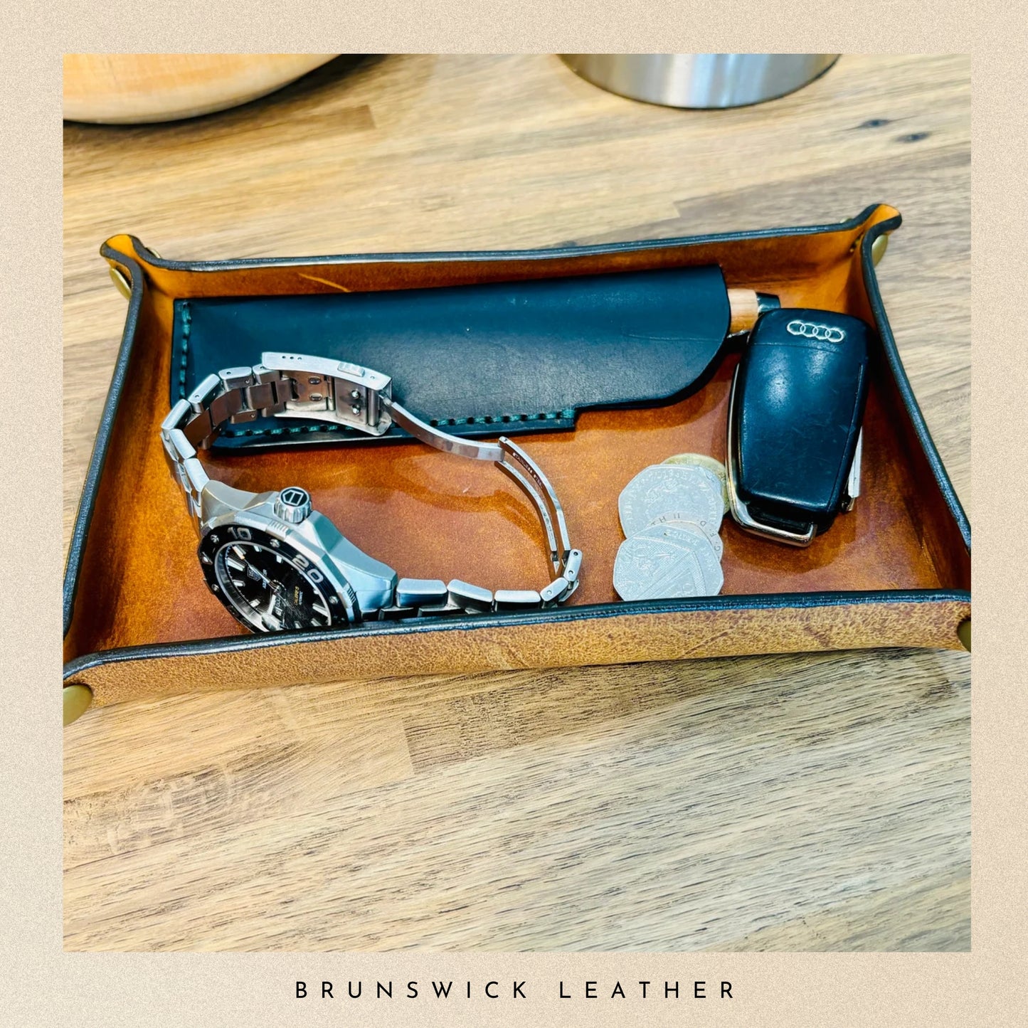 Leather tray with a watch, car key, and sunglasses on a wooden surface, branded 'Brunswick Leather'.