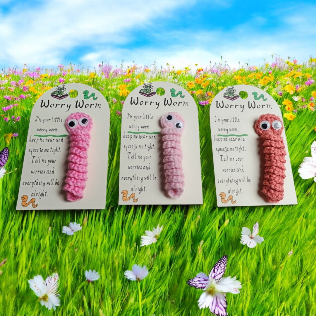 Three pink worry worms on cards with a poem against a grass and flowers background